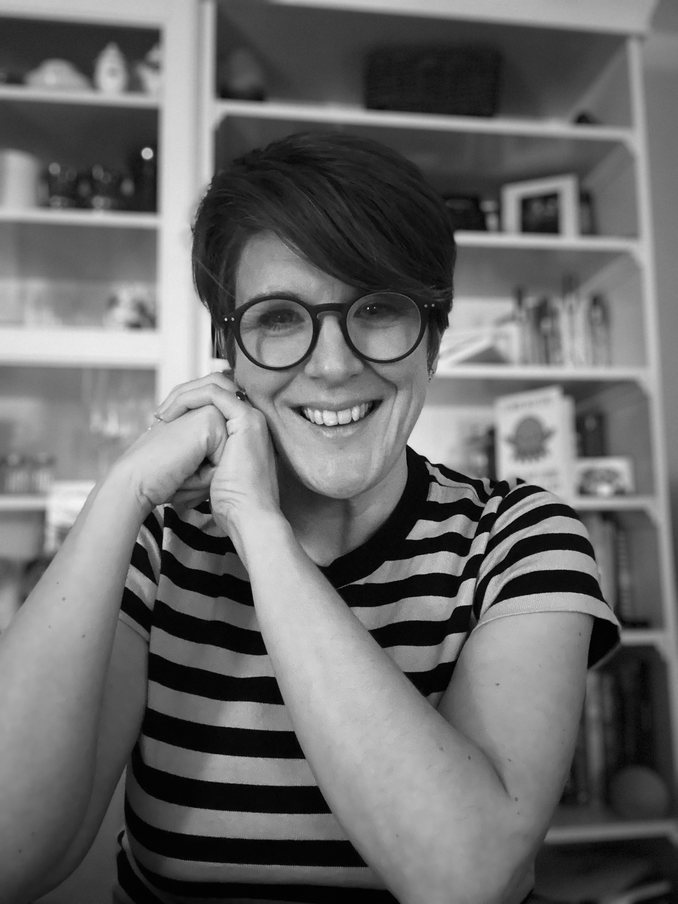This is a black and white photograph of Heather. She is smiling into the camera, she wears a pair of black spectacles and a striped T-shirt. 